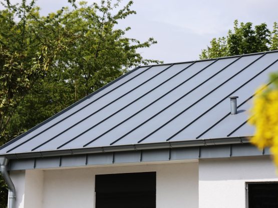 A residential house features a durable, light gray aluminum roofing with standing seams under a bright sky.